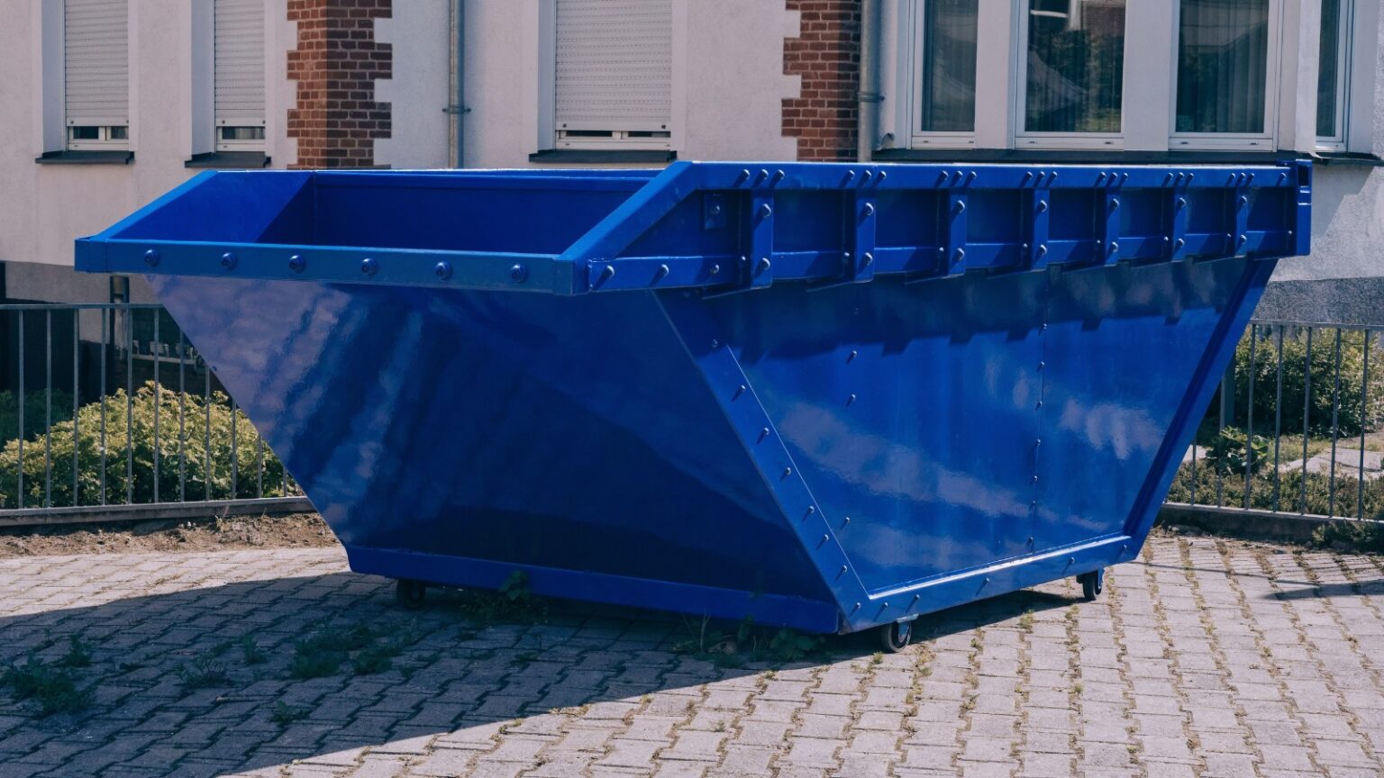 Leere blaue Absetzmulde vor einem Wohnhaus, mietfertig – Mulde mieten in Wien, Niederösterreich und Burgenland