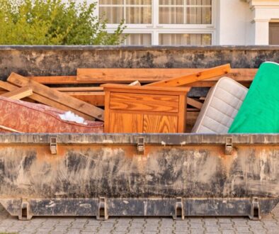 Absetzmulde auf einer Einfahrt, gefüllt mit Sperrmüll wie altem Sofa, Holzschrank, Matratze und Altholz