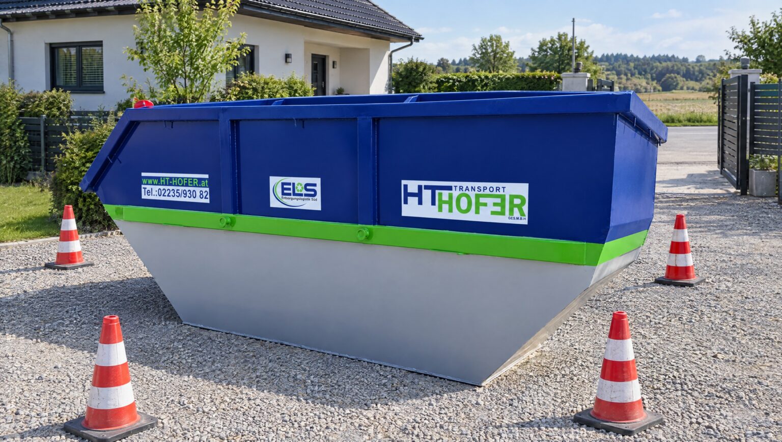 Blaue Absetzmulde steht aufstellbereit in einer gepflasterten Hofeinfahrt, daneben die offene Durchfahrt mit Torpfosten